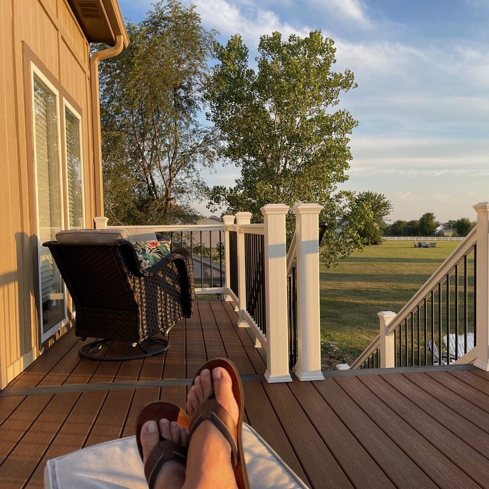 elevated backyard deck with white railings overlooking grassy yard and wicker patio chair in sunlight