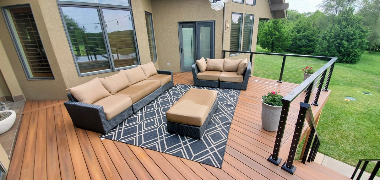 outdoor deck with wood planks black cable railings and patio furniture overlooking a grassy backyard
