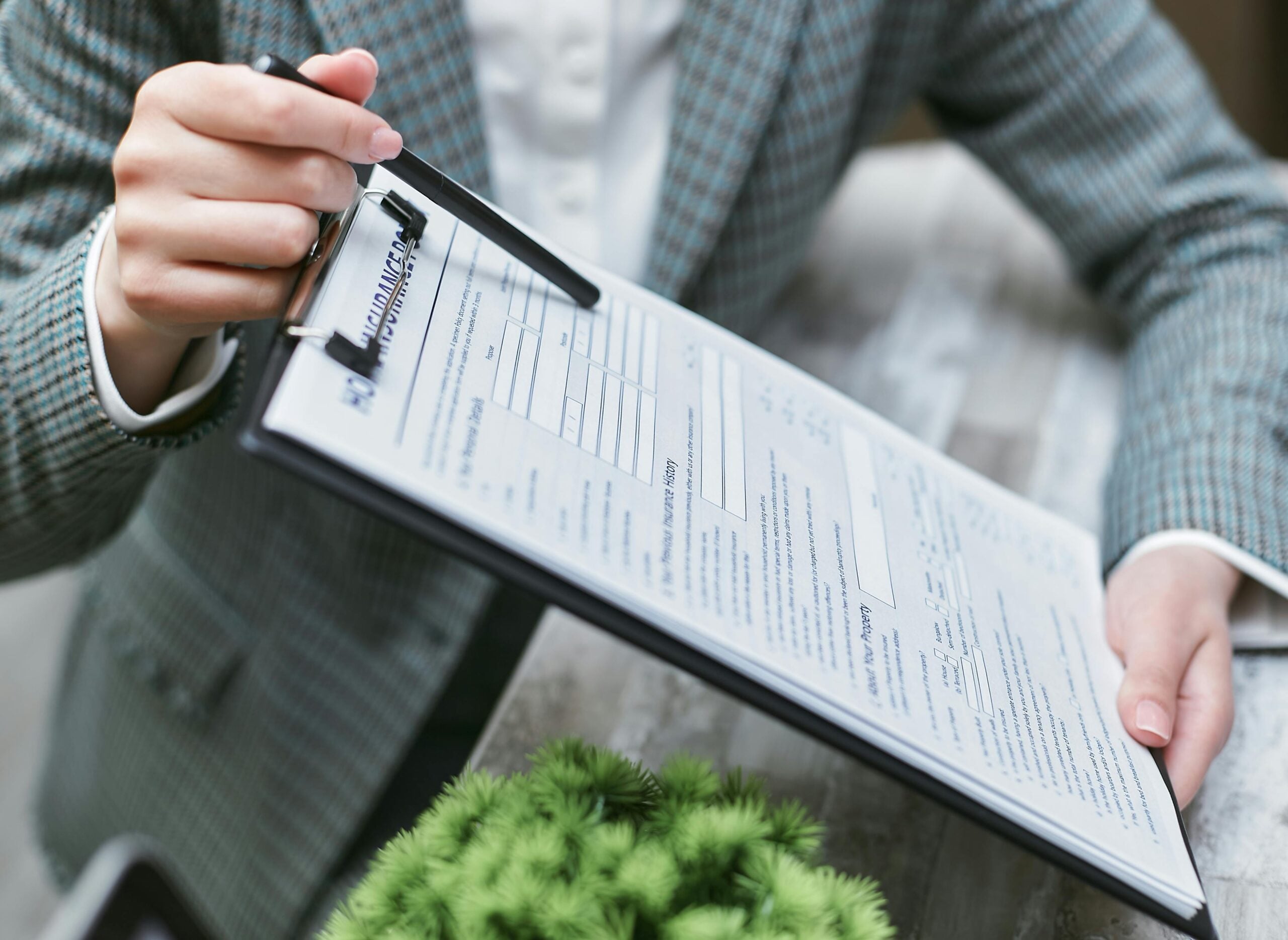 person reviewing a printed contract document on a clipboard at a table with a small green plant nearby