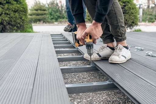 worker using power drill to fasten composite deck boards onto metal framing outdoors