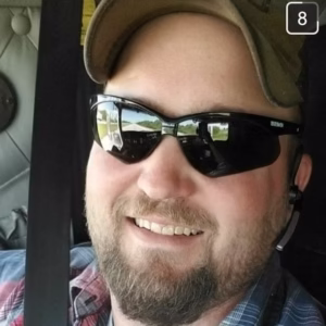 Man smiling while sitting inside a vehicle wearing sunglasses and a cap