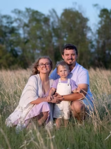 Three people posing together in tall grass with trees and blue sky in the background