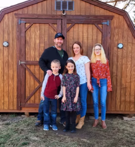 family standing on grass in front of wooden backyard shed with double doors and small vent above
