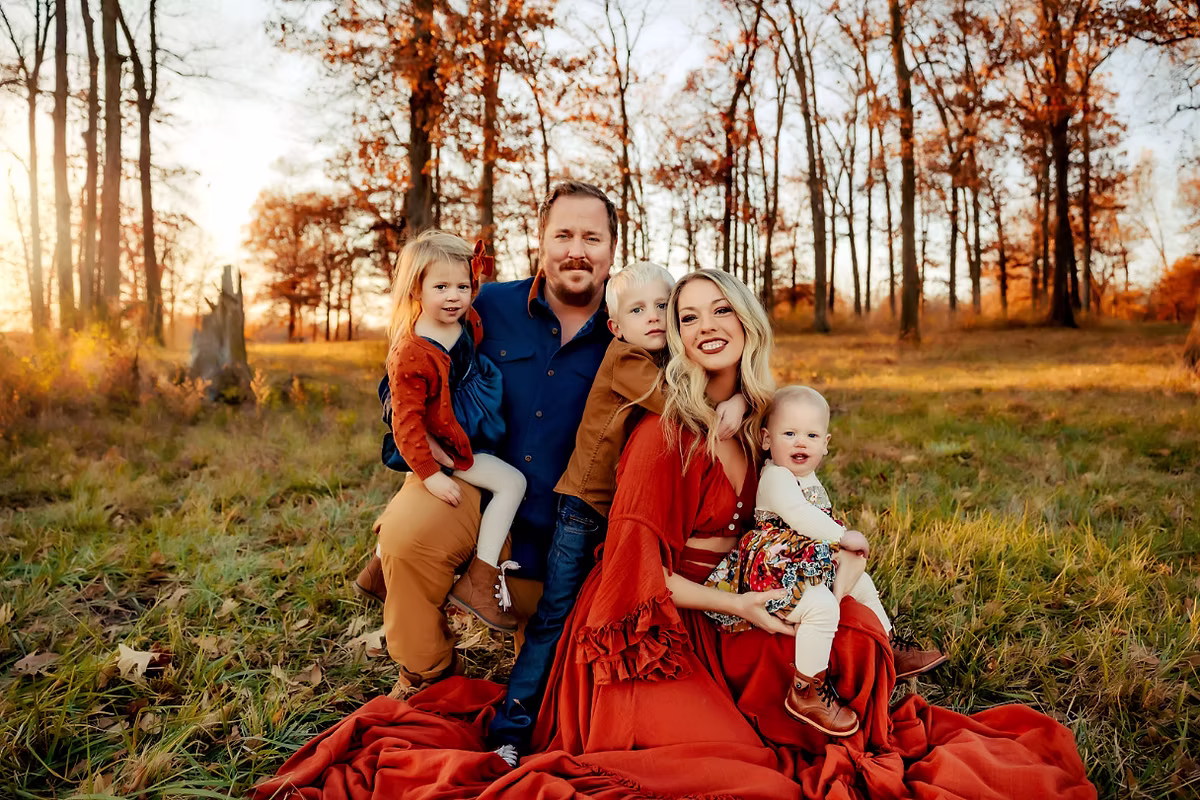 family sitting on blanket in grassy woodland with autumn trees in warm evening light