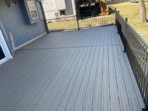Spacious elevated gray deck with evenly aligned boards and black metal railings overlooking a backyard lawn