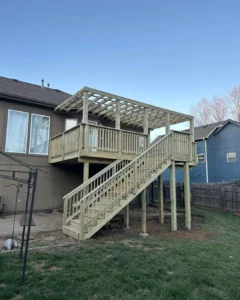 wooden elevated deck with railing, pergola frame, and staircase extending to backyard lawn