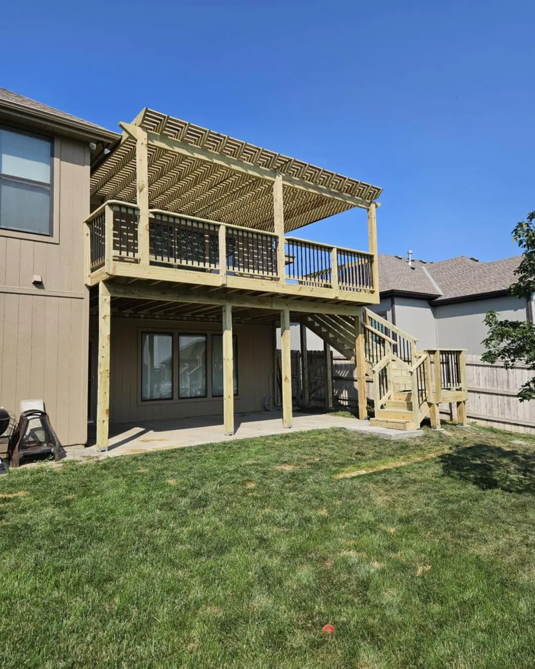 elevated wood deck with pergola overhead and staircase leading to backyard showing custom deck design ideas